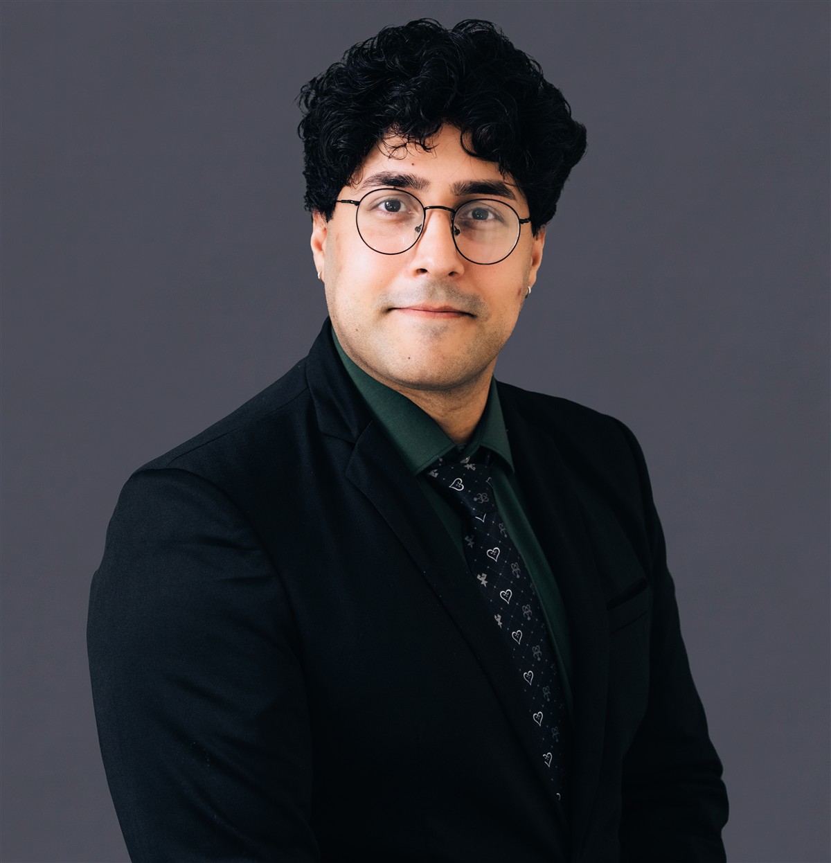 Danish Idrees wearing glasses, a dark suit, and a forest-green shirt
